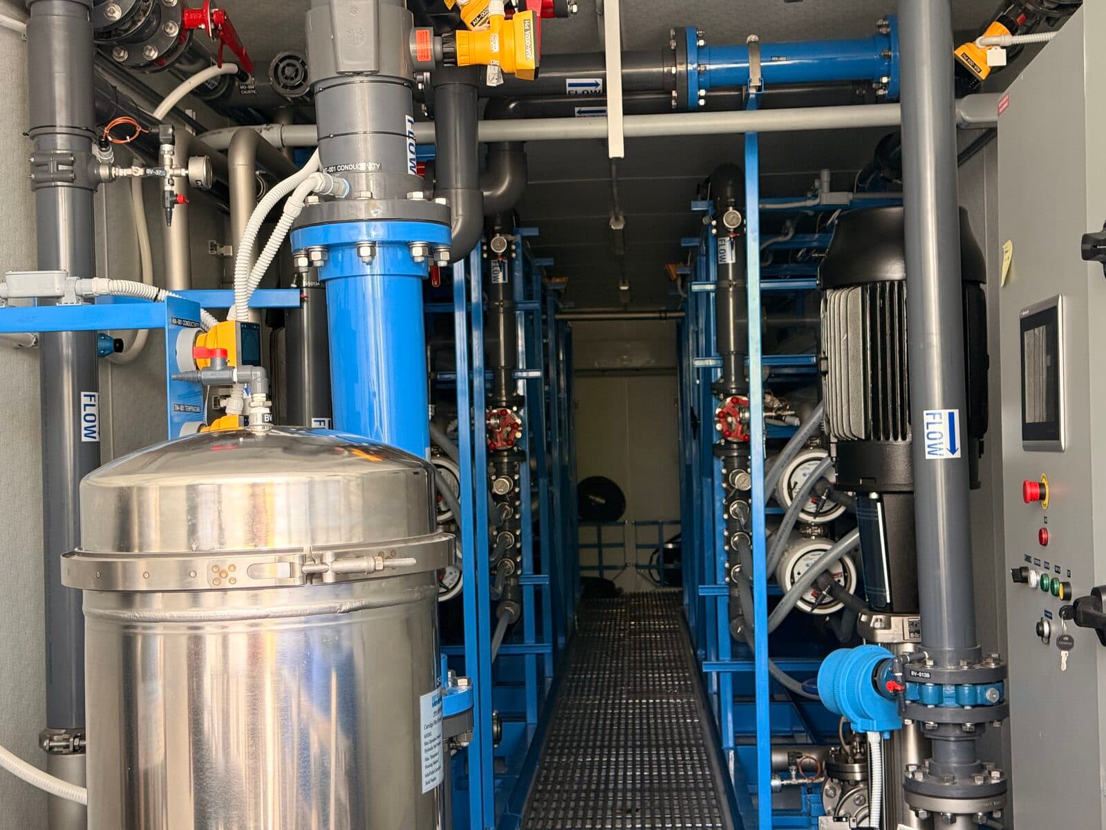 Inside containerized RO water treatment system at Falcon Water Tech — blue pumps, stainless steel filtration vessels, and membrane housings